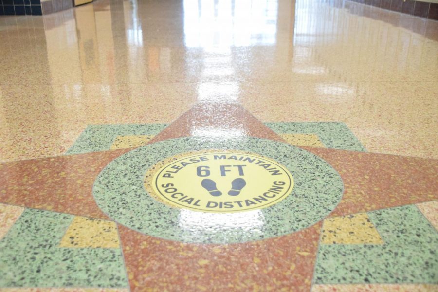 Signs+on+the+hallway+floors+remind+students+to+remain+socially+distanced.